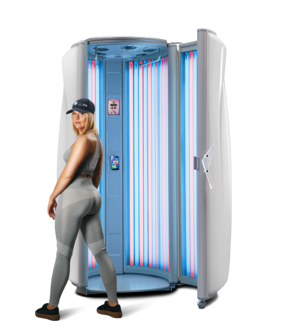 An Ultrasun E6 stand-up tanning booth with an open door showing CollaTan and UV lamps. A woman in grey gym leggings and a baseball cap stands with her back to the camera, looking over her shoulder toward the machine.
